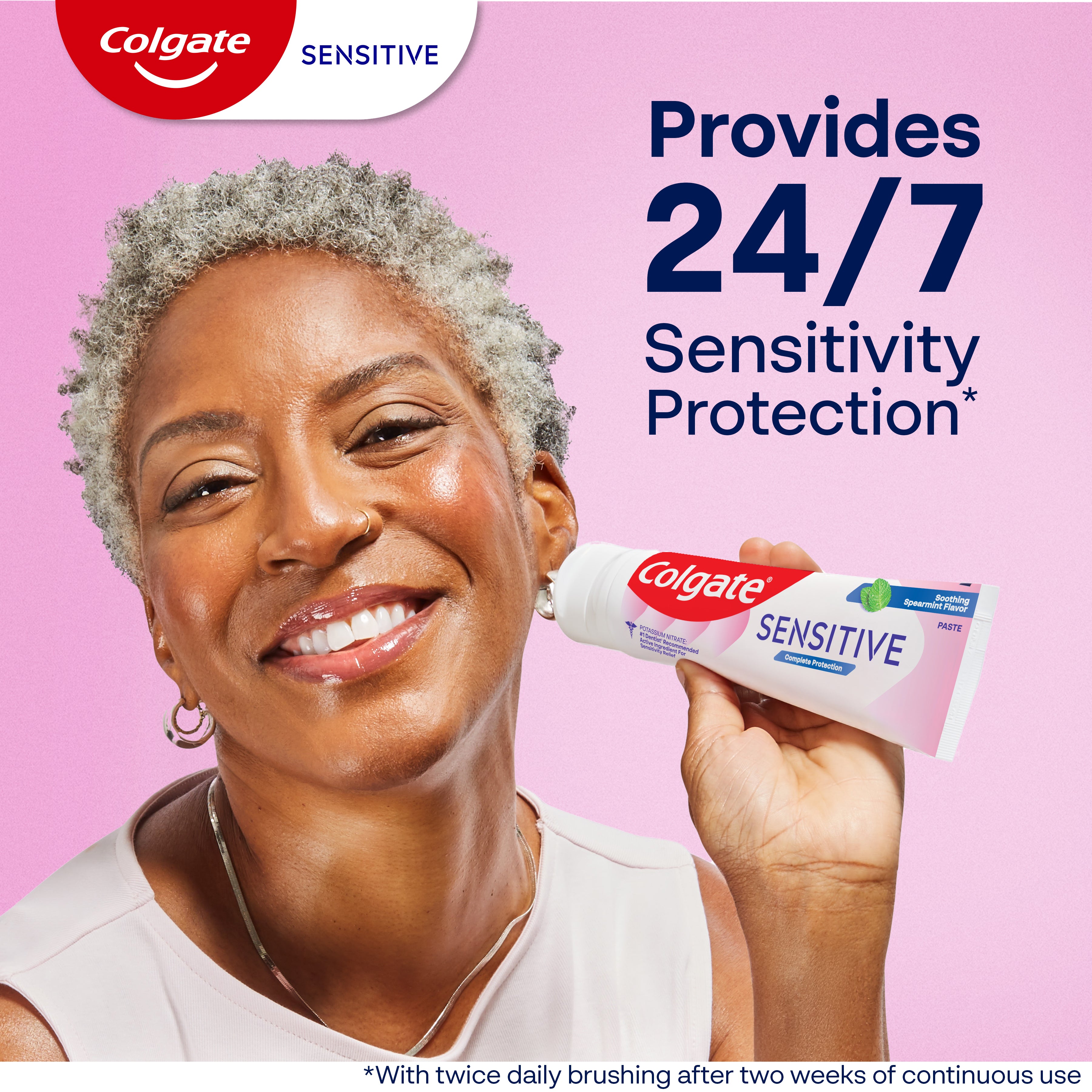 A woman smiling holding a tube of Colgate Sensitive Complete Protection Toothpaste. In text: Provides 24/7 sensitivity protection*. *With twice daily brushing after two weeks of continuous use.