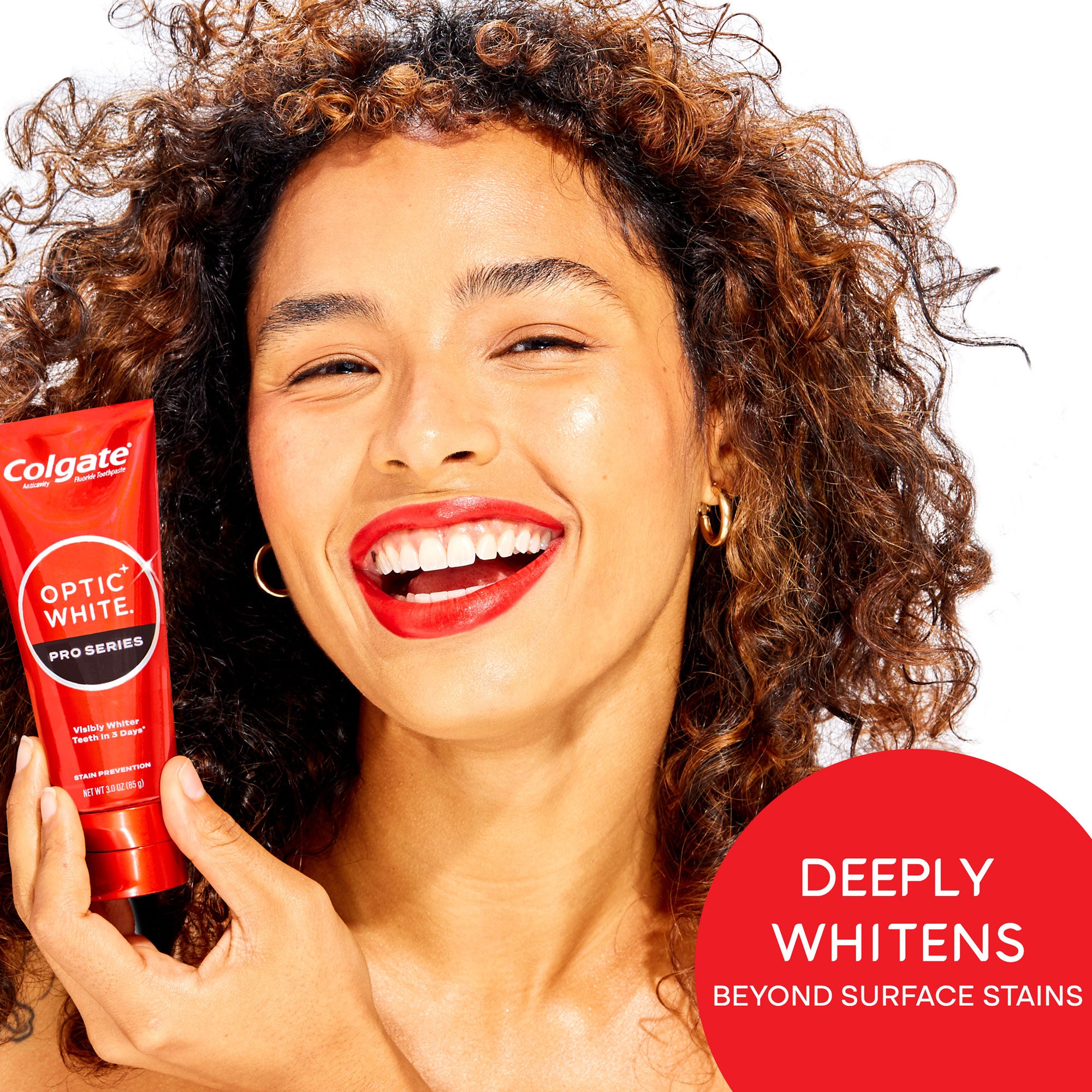 A woman smiling holding a tube of Colgate Optic White Pro Series Stain Prevention Whitening Toothpaste. In text: Deeply whitens beyond surface stains.
